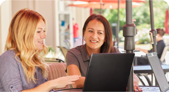 A female mentor and mentee at ADT sit together, talking and working on a laptop.