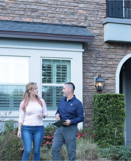 A male ADT Sales Rep stands outside a house talking with the female homeowner.