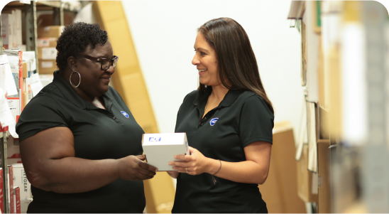 Two female ADT Field Operations employees stand together, looking at an ADT product in a box that one of them is holding.