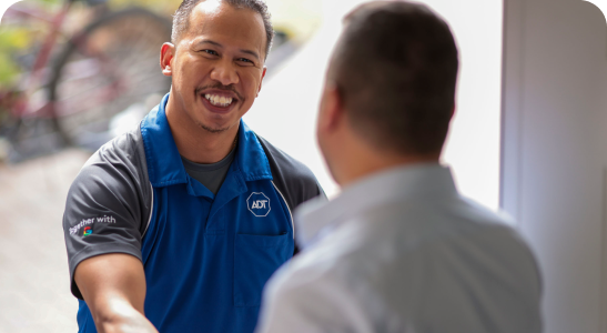 A male ADT Field Operations employee smiles as he shakes hands with a homeowner.