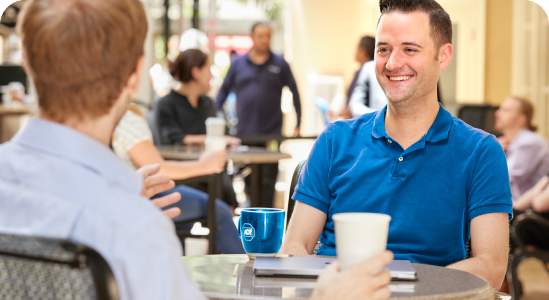 Two male ADT interns sit talking together over coffee.