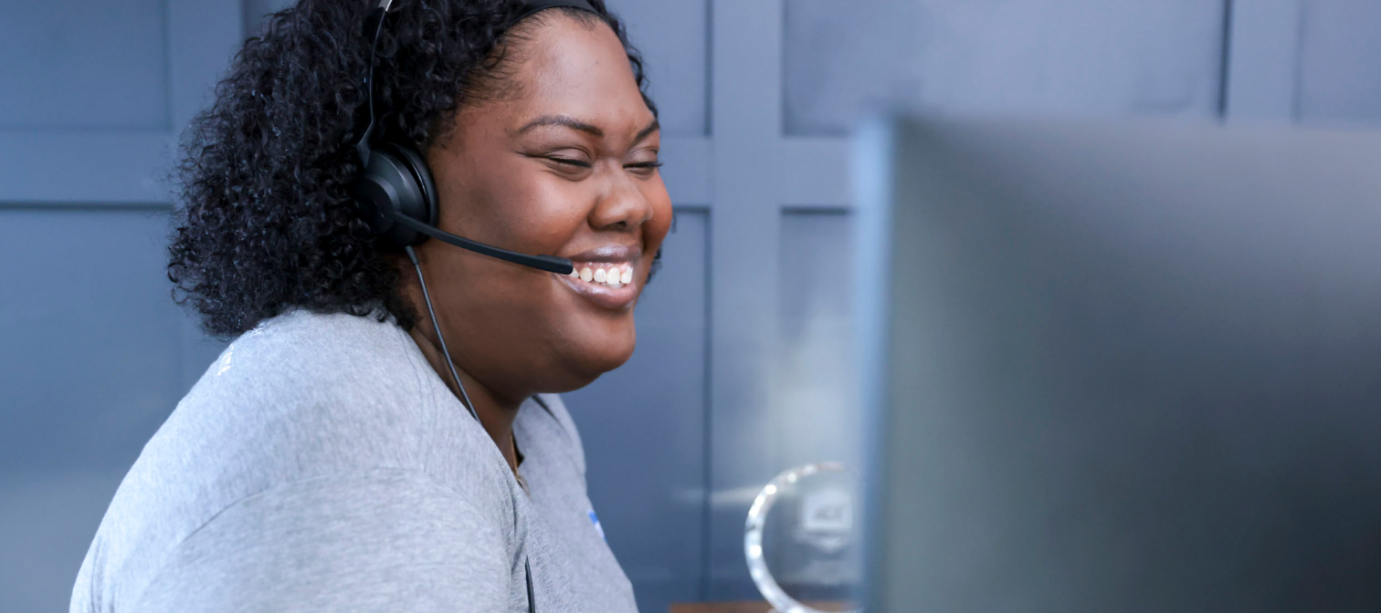 An ADT Customer Technical Support employee smiles as she talks into the mouthpiece on her headset.
