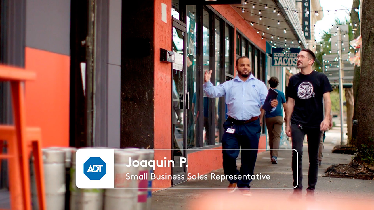 Joaquin, an ADT Small Business Sales Representative, talking to another man while walking in front of multiple storefronts on the sidewalk