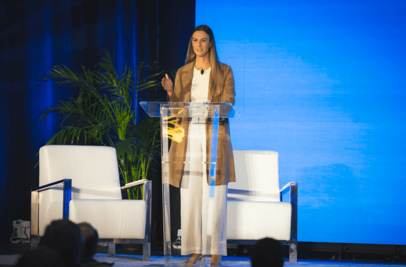 nicole speaking onstage at a clear adt podium in front of a blue screen